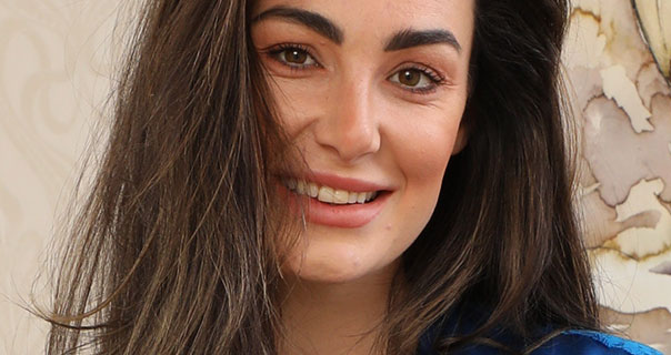 Tanya T appears against an off-white background. She smiles wearing blue satin. Her brown hair is loose and partly covers her face.