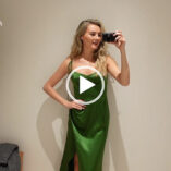 Niomi Smart films herself in medium size beige wall changing room. Niomi has her long hair loose and in waves. She wears a long green split skirt dress with fresh and natural looking makeup.