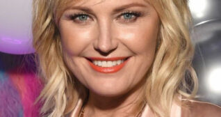 Malin Akerman wears a baby pink satin blazer. She looks forwards and smiles with her hair loose around her shoulders.