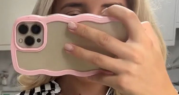 Em Sheldon holding her iPhone front of her face as she vlogs. Em is wearing a white and black stripe shirt from LilySilk.