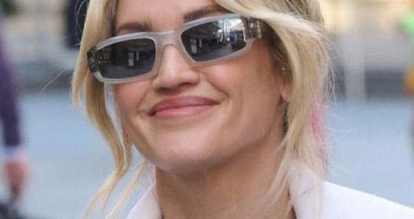 Ashley Roberts wears a white coat with a pair of translucent frame sunglasses. Her hair is tied up with a few strands pulled down around her face.