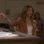 India de Beaufort hands a gavel to Melissa Rauch in a courtroom with the jury behind her. She wears a blazer and a white satin camisole top.