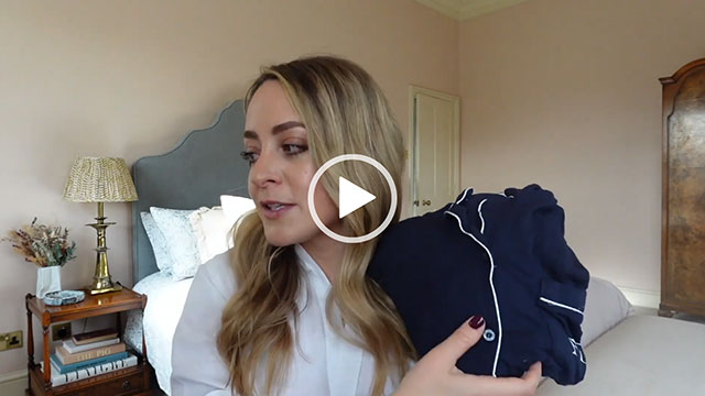 Fleur Bell holds up a pair of navy and white piping cotton pyjamas. She appears in one of her bedrooms and wears a white shirt with her hair loose.