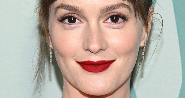 Leighton Meester is seen in front of a green background. She wears her hair up with a dark red lipstick and thin dangling earrings.