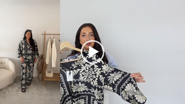 Hazel Maria Wood is seen in two split frames. She holds a black and white satin top in one and is wearing the top with matching satin trousers in the second. Hazel appears in front of a cream wall and next to a wooden clothes rack in her white and grey filming room.