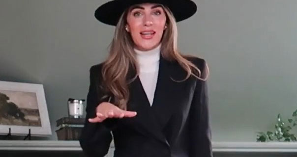 Lydia Elise Millen is seen in her sage green wardrobe room. She wears a cream high neck jumper with a black large brim hat and a black blazer.