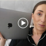 Hazel Maria Wood props herself up on her bed. She a navy pyjama top as she rests against white pillows. Hazel has her hair tied back as she holds up her silver MacBook with one hand.