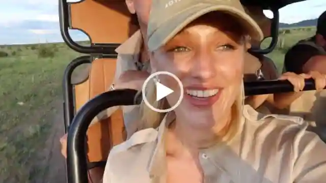 Leonora Smee rides in a black metal frame and orange leather open jeep on safari in Africa. She wears a baseball cap with a shiny LilySilk shirt. Leonora is seen in minimal makeup with her blonde hair loose and straight. She looks forward into the setting sun with a grassy plain around her.
