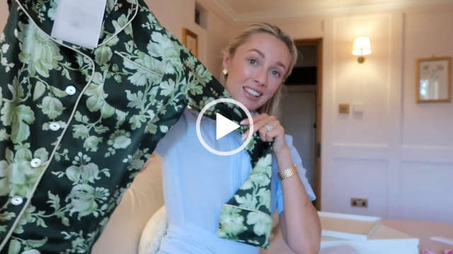 Josie Irons holds up a dark and light green floral satin pyjama top. She sits in a white bedroom at her home in the Cotswolds. Josie wears a blue short sleeve dress. She has her long blonde hair tied back and is seen in a pair of small earrings and a matt pink lipstick.