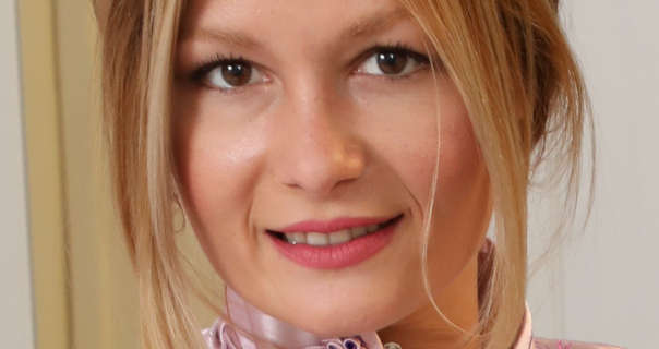 Freya H wears a dark pink matt lipstick and black mascara. She appears in front of a white wardrobe. Freya has blonde highlights with her hair tied up and back in a bun. She is seen in a dark pink satiny Chinese dress.
