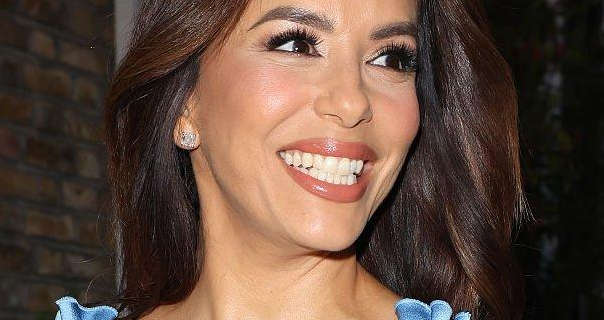 Eva Longoria appears at night in London. She arrives at a restaurant with her dark brown hair loose and in soft waves. Eva smiles widely. She wears a dark pink gloss pink lipstick with black mascara, jewel stone earrings and a light blue dress.