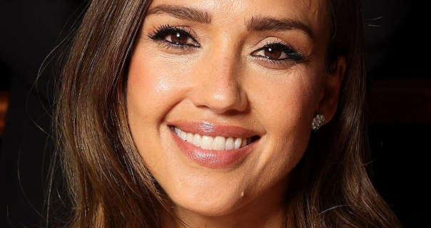 Jessica Alba wears her light brown hair down, long and slightly wavy. She appears in a dark room. Jessica is seen in a pink gloss lipstick, a pair of flower head jewel stone earrings and black mascara.