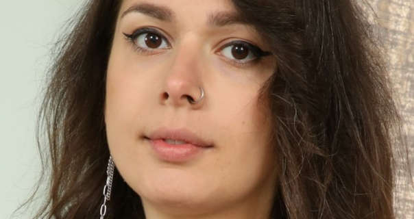 Gia wears her black hair loose and frizzy. She stars in a light pink lipstick, black eyeliner and black mascara. Gia is seen in front of a pale green wallpaper and shimmery cream curtains. She a pair of dangling silver earrings with her silver nose ring.