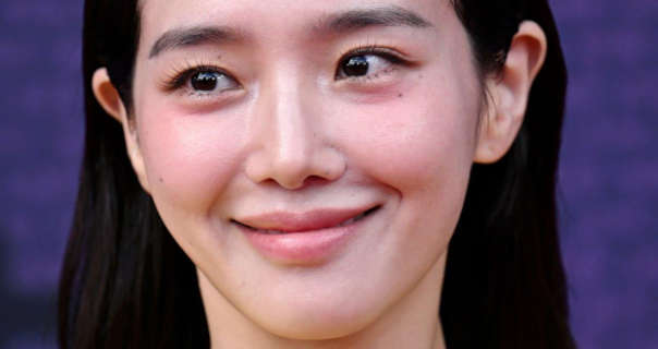 Park Gyu-young appears in front of a dark purple wall. She wears her black hair down, loose and tucked behind both ears. Park Gyu-young stars in black mascara and a light pink sheen lipstick.
