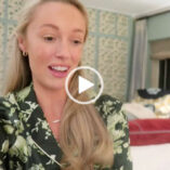 Josie Irons sits in a red, cream and green bedroom during a retreat in the Cotswolds. She wears her long blond hair loose and pushed back. Josie is seen in a pink lipstick, small gold earrings and a pair of flower print dark and light green long sleeve pyjamas.