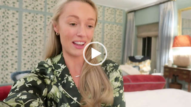 Josie Irons sits in a red, cream and green bedroom during a retreat in the Cotswolds. She wears her long blond hair loose and pushed back. Josie is seen in a pink lipstick, small gold earrings and a pair of flower print dark and light green long sleeve pyjamas.