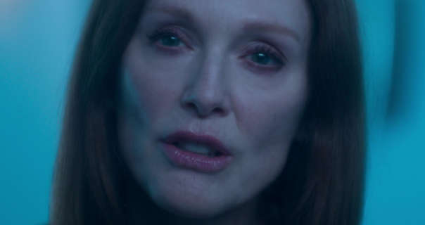 Julianne Moore is seen in a blue and black ethereal lit bathroom with a haunted expression. She wears her long hair down and loose. Julianne is seen in a red lipstick, red blush and soft black mascara.