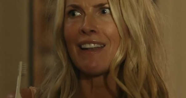 Ali Larter is seen looking puzzled while holding a white toothbrush in one hand. She wears her long blonde hair down and in waves. Ali stands in dark beige bedroom. She is seen in a glossy pink lipstick and minimal foundation.
