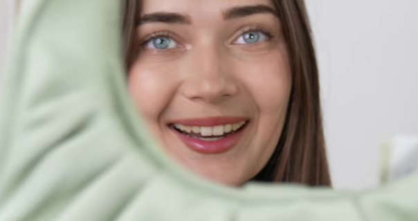 Roxxsaurus holds up a light green ASOS bag and looks through it into the camera. Roxi is seen in front of a dark white wall. She has her long light brown hair straightened and loose. Roxi wears a dark pink lipstick with mascara and a matt foundation.