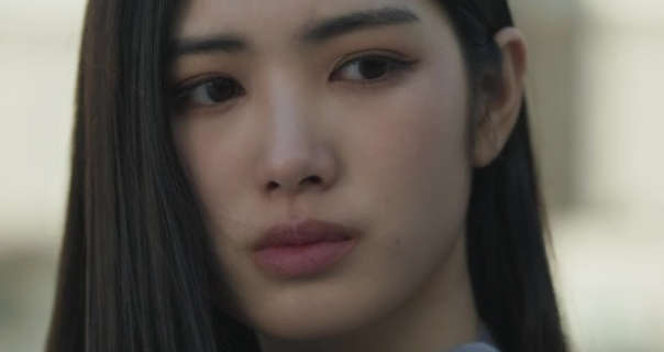Regina Lei is seen outside on a roof terrace with light colour buildings behind her. She wears her black long hair straightened, loose and tucked behind one ear. Regina stars in a matt foundation, soft blush, pink lipstick and black eyeliner.