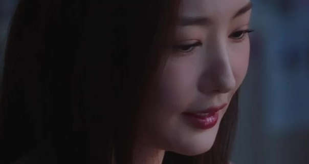 Park Min-young is seen with her long black hair loose and straightened framing her face. She sits in a dark room looking downwards . Park Min-young wears foundation with a dark red gloss lipstick.