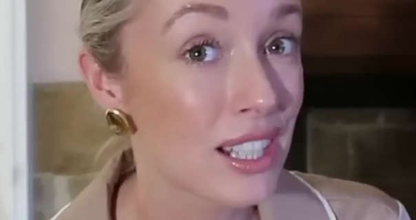 Josie Irons is seen sitting in front of one of her large dark wood fireplaces in her Cotswolds home. She wears her blonde hair tied up and back. Josie appears in a pair of champagne gold pyjamas, a glossy lipstick, black mascara and a pair of gold solid circle earrings.