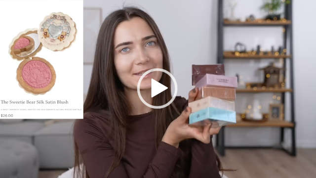 Roxxsaurus holds up five different blush palettes from Flower Knows. She sits in her tiny home filming studio set in front of a grey couch and wood ladder display shelves. Roxi wears a dark brown thin long sleeve top. She is seen with her long hair loose and straightened and with no makeup on.