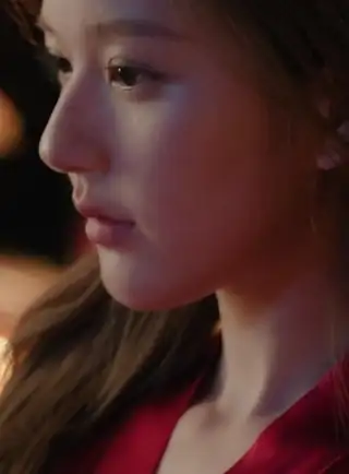 Zhao Lusi is seen outside at night lit in orange lamplight. She has her long black hair loose as she gazes forwards while deep in thought. Zhao Lusi wears a red dressing gown with minimal makeup.