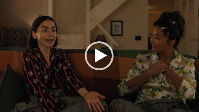 Ashley Park sits alongside Lily Colins on a long couch in front of a narrow white wood staircase and an open door. She wears a pair of white, yellow and green lemon print pyjamas. Ashley is seen with her black hair pinned up with a few pink hair clips. She stars in a little makeup and a pair of hanging earrings.