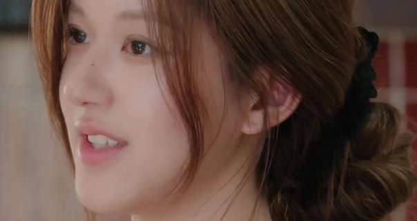 Zhao Lusi appears in an open plan flat living room. She is seen from the side with her long hair tied in a low bun and minimal makeup.