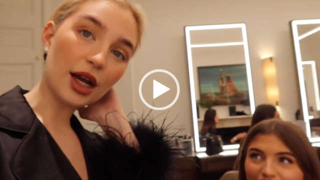 Grace Shadrack is seen next to Grace Foley as they get ready in a backstage dressing room. They vlog in front of a row of long illuminated makeup mirrors and dark wood tables. Grace and Grace wear black feather trim pyjamas.