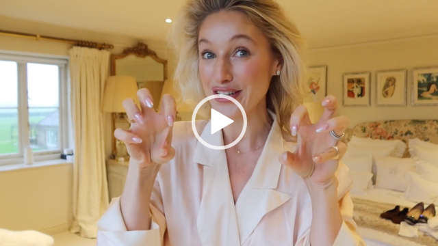 Leonora Smee stands in her large neutrally decorated dressing bedroom at her home. She stands near the window and in front of a bed that has several pillows and pairs of shoes across it. Leonora has her long blonde hair pushed back. She holds up both hands to the camera to show her manicured nails.