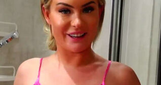 Louise Jones stands in front of a chrome and cream tile shower cubicle. She wears her long blonde hair tied back. Louise is seen in pink nightwear, matt foundation and mascara.