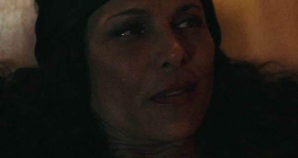 Francisca Dennis looks up and to one side and smirks. She rests against a large gold pillow. Francisca has her black hair loose and in tight curls. She is seen in foundation, blush, mascara and a dark pink lipstick.