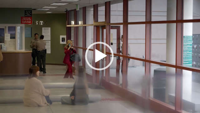 Becki Newton is seen at a distance as she walks through a large open plan green police foyer. She wears a dark pink suit and carries a phone and a large leather bag in her hands. Becki has her long blonde hair loose and styled in waves. She heads towards an opening door.