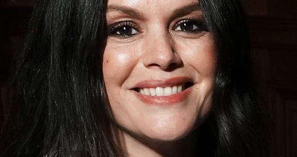 Rachel Bilson appears in the dark at a nighttime event. She wears her long black hair loose and styled naturally. Rachel stars in a soft matt foundation, black mascara and a red lipstick.