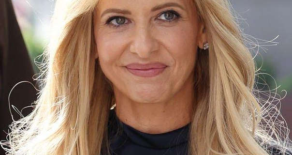 Sarah Michelle Gellar is seen outside in the sunshine with her blonde hair loose and blowing a little in the wind. She wears a dark navy top with a pair of diamond earrings. Sarah is seen in mascara, dark pink lipstick and a matt foundation.