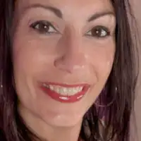 Vana is seen with her shoulder length hair loose and straightened. She takes a selfie ahead of one of her livestreams. Vana wears a glossy lipstick with black eyeliner, mascara and a pair of thin large gold hoop earrings.
