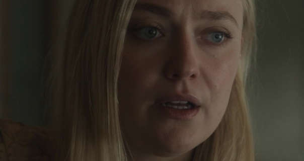 Dakota Fanning appears in a dark room in front of a dark sage wall. She wears her long blonde hair straightened and loose. Dakota stars in a matt foundation, curled lashes and a dark pink lipstick.