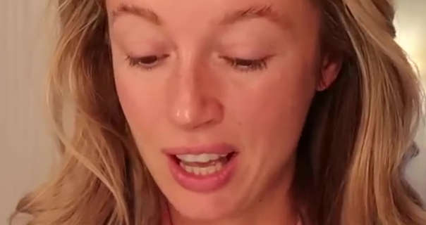 Josie Irons stands near the white doorway of a bathroom in a countryside retreat. Her long blonde hair is in loose natural curls. Josie is seen looking downwards as she speaks. She wears no makeup as she starts a morning skin care routine.
