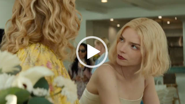 Anya Taylor-Joy is seen in a light and airy open plan living room space. She has her blonde hair cut to shoulder length. Anya leans forwards and looks towards Annie Tedesco. She wears a white dress with a matt foundation and a dark mauve lipstick.