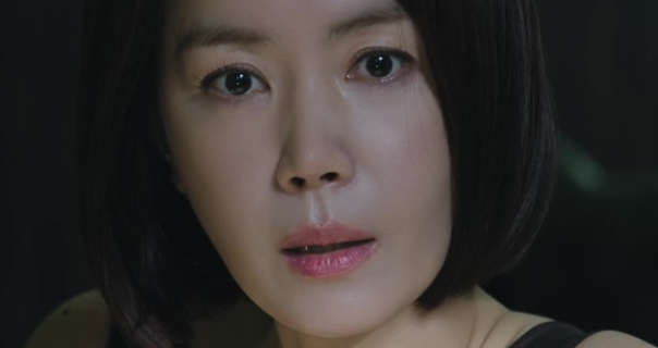 Kim Yu-mi is seen with her short black hair loose and framing her face. She appears in a dark bedroom looking forward with a thoughtful look. Kim Yu-mi wears a smooth foundation with mascara and a pale pink lipstick.