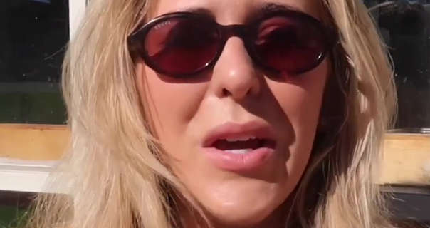 Em Sheldon is seen sitting outdoors in the sunshine as she explores Nantucket. She has her thick blonde hair styled naturally and loose. Em wears a pair of oval sunglasses as she speaks to the camera. She wears a heavy foundation with a soft blush and plumping pink lipstick.
