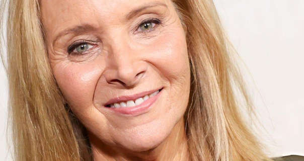 Lisa Kudrow is seen in front of a dark white wall. She has her shoulder length blonde hair straightened and loose. Lisa wears a light foundation with pale blush, mascara and a pink lipstick.
