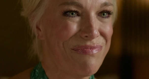 Hannah Waddingham smiles and looks forwards wistfully. She has her blonde hair tied back in a bun. Hannah is seen in a green halter neck dress, light foundation, flushed checks, black mascara and a pair of stud earrings.