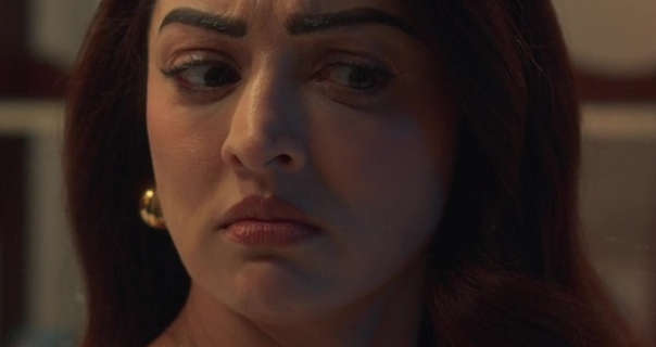 Sandeepa Dhar is seen in a dark room under a yellow lamplight. She has her long black hair loose and with a red tint. Sandeepa wears a pair of chunky gold earrings with a little foundation, mascara and a dark pink lipstick.