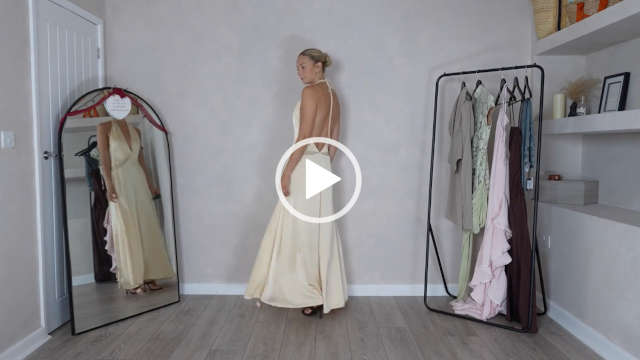 Emily Wilson Fashion stands in front of a light grey wall at her home during a try on haul. she wears a backless light yellow PrettyLittleThing dress. Emily is seen from the side as she turns. She wears her long blonde hair tied in a tight bun.