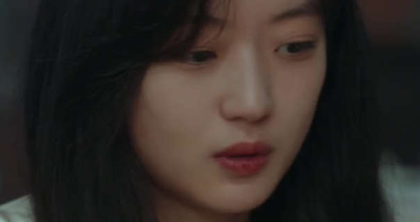 Sun Qian sits in an indoor eating area and looks thoughtful. She has her long black hair loose , straight and with a bit of a fringe. Sun Qian wears a light gold shirt with foundation, natural eyes and a red lipstick.