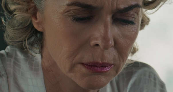 Margarita Rosa de Francisco appears in front of a large apartment window during the day. She is seen close up with her eyes mostly closed. Margarita wears a light foundation with mascara and a pink gloss lipstick.